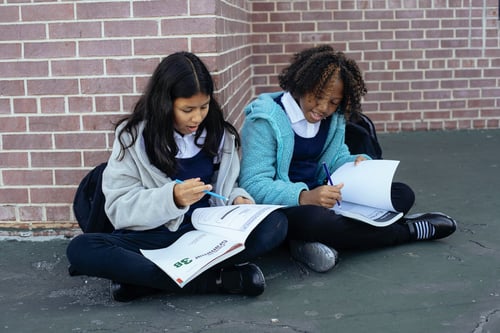 Two pupils in uniforms sitting on the ground, reading books